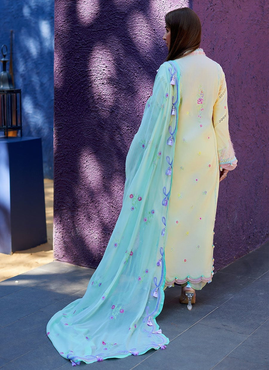 A woman wearing a light yellow embroidered kurta with a mint green dupatta, photographed from behind against a textured purple wall.