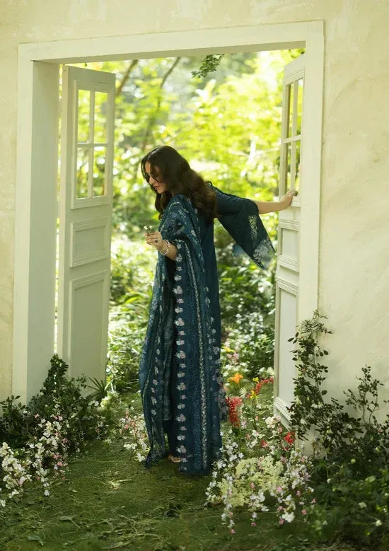 Woman in a blue dress standing in a garden with open doors.