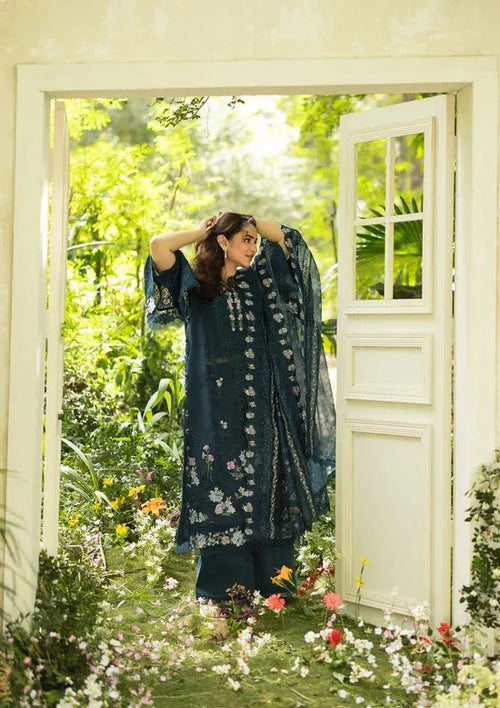 Woman in a floral dress standing in a garden with flowers and greenery.