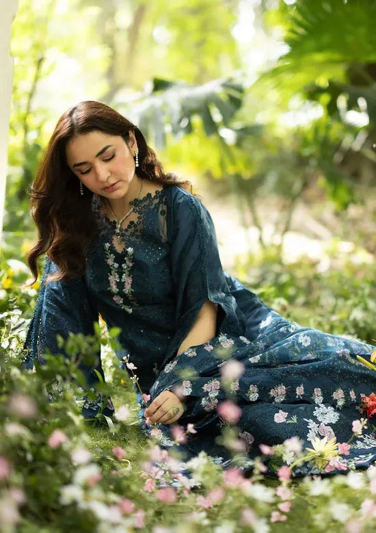 Woman in a blue embroidered dress sitting among flowers and greenery