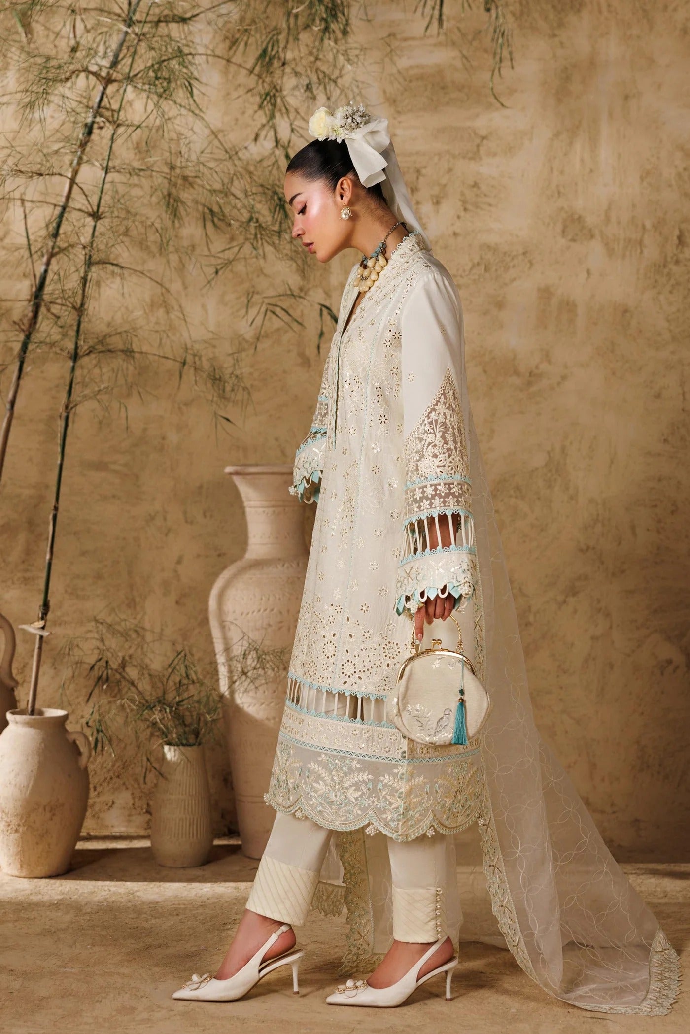 Woman in a traditional outfit with intricate designs standing against a textured wall.