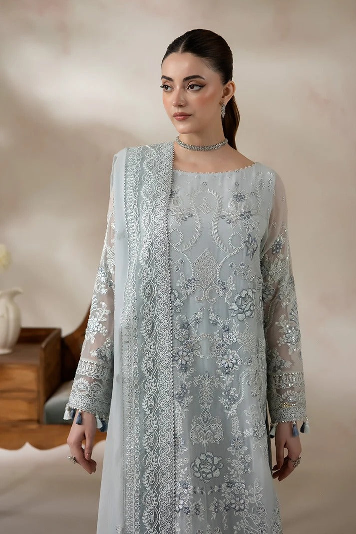 A woman models a light blue-gray traditional embroidered kurta set with matching sheer dupatta and silver embellishments, set against a soft beige background.