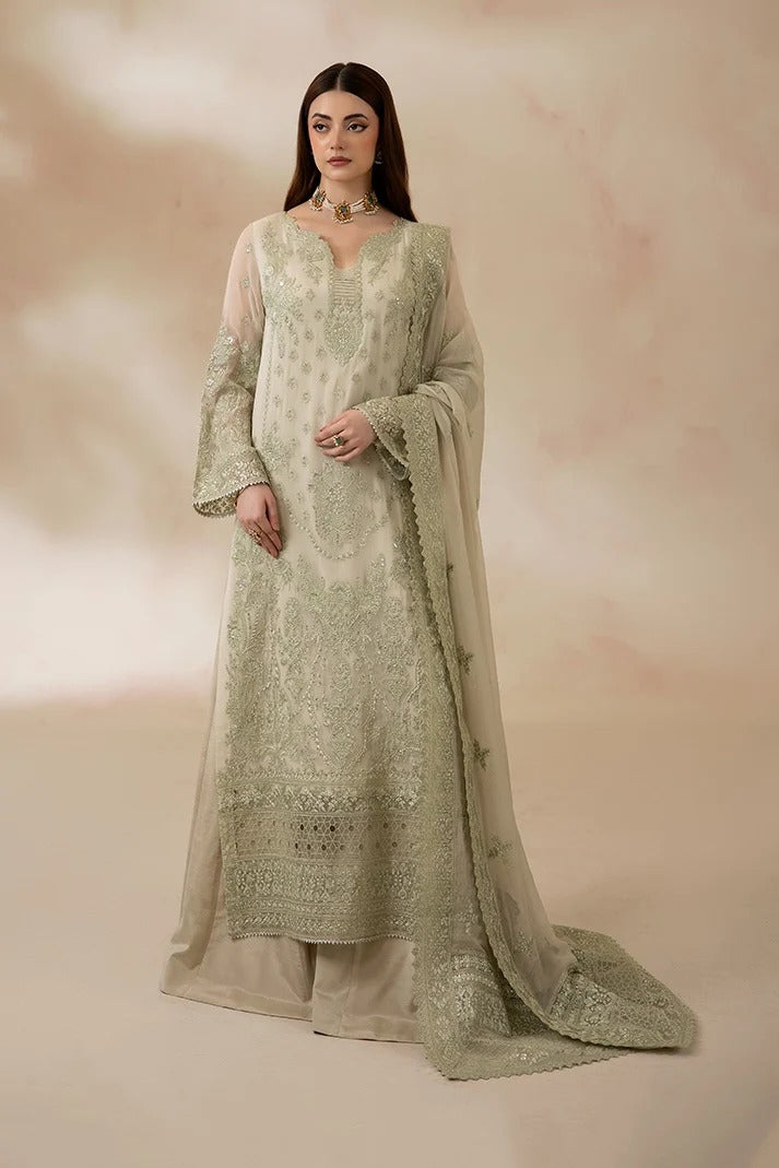 A woman models a traditional South Asian outfit featuring a light sage green embroidered kurta with matching sheer dupatta and wide-leg trousers, set against a soft beige studio backdrop.