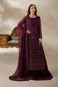 A woman models a deep plum purple embroidered traditional outfit with a matching sheer dupatta, set against a warm beige studio backdrop with a wooden chair.