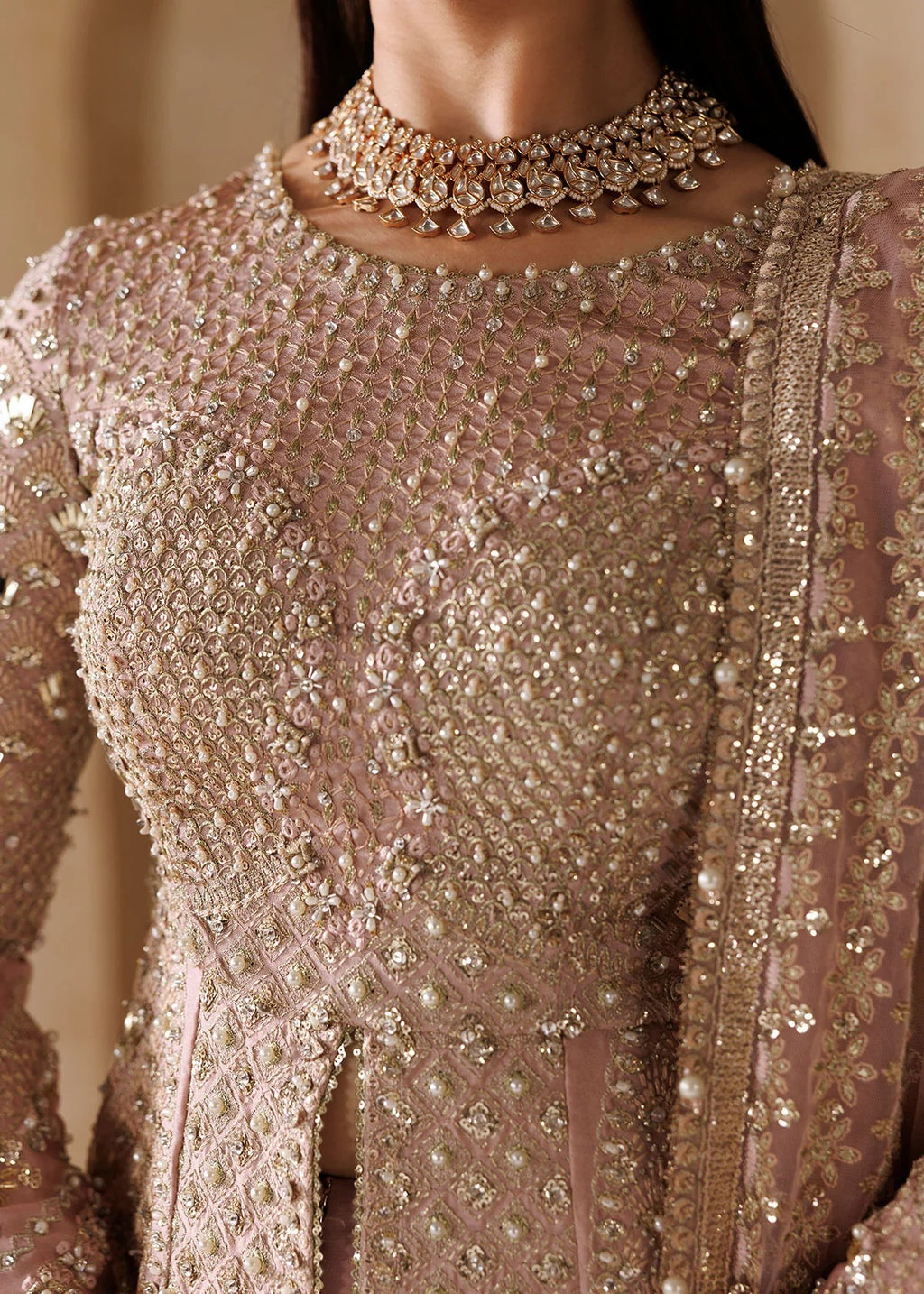 Close-up of a model wearing a heavily embellished dusty rose pink traditional outfit with intricate gold and silver beadwork, embroidery, and a matching beaded choker necklace.