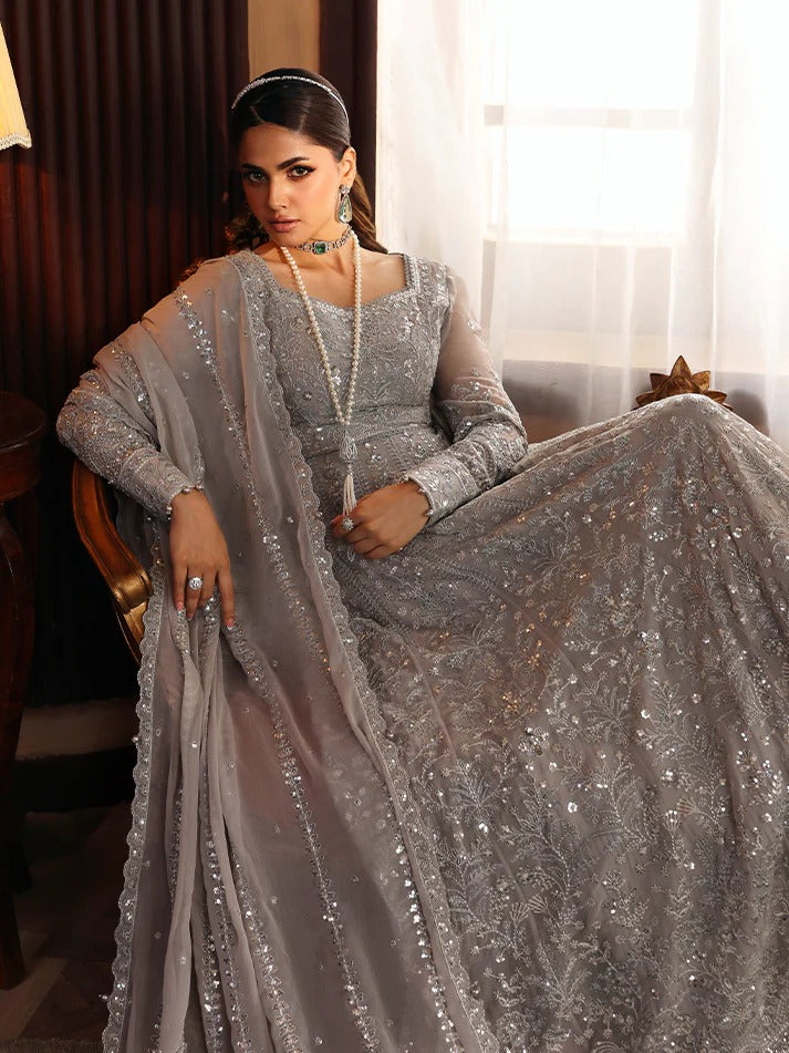 Woman in a silver embroidered traditional outfit sitting on a couch.