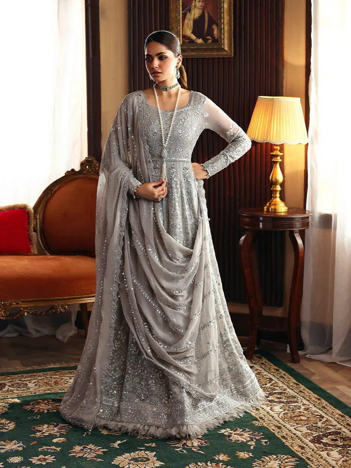 Woman in a silver saree standing in an elegant room with a lamp and sofa.