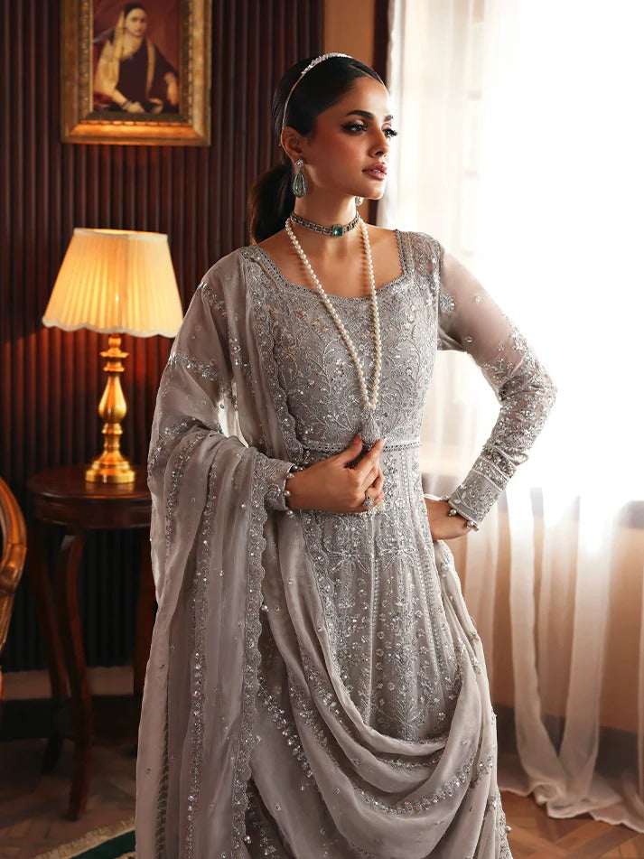 Woman in a silver traditional outfit standing in a room with a lamp and painting in the background.