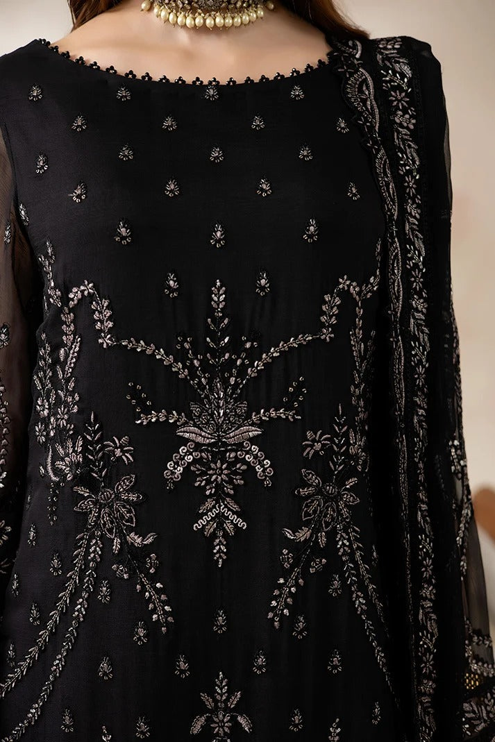 A close-up of a black embroidered traditional outfit with intricate silver mirror-work embroidery, sheer sleeves, and a scalloped neckline, shown on a model wearing a gold necklace.