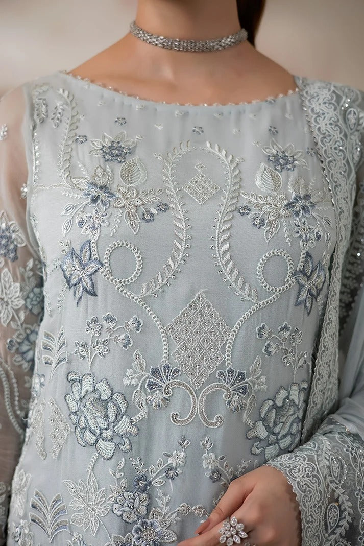 A close-up of a model wearing a light blue-grey traditional embroidered dress with intricate silver and white floral embroidery, paired with a silver choker necklace.