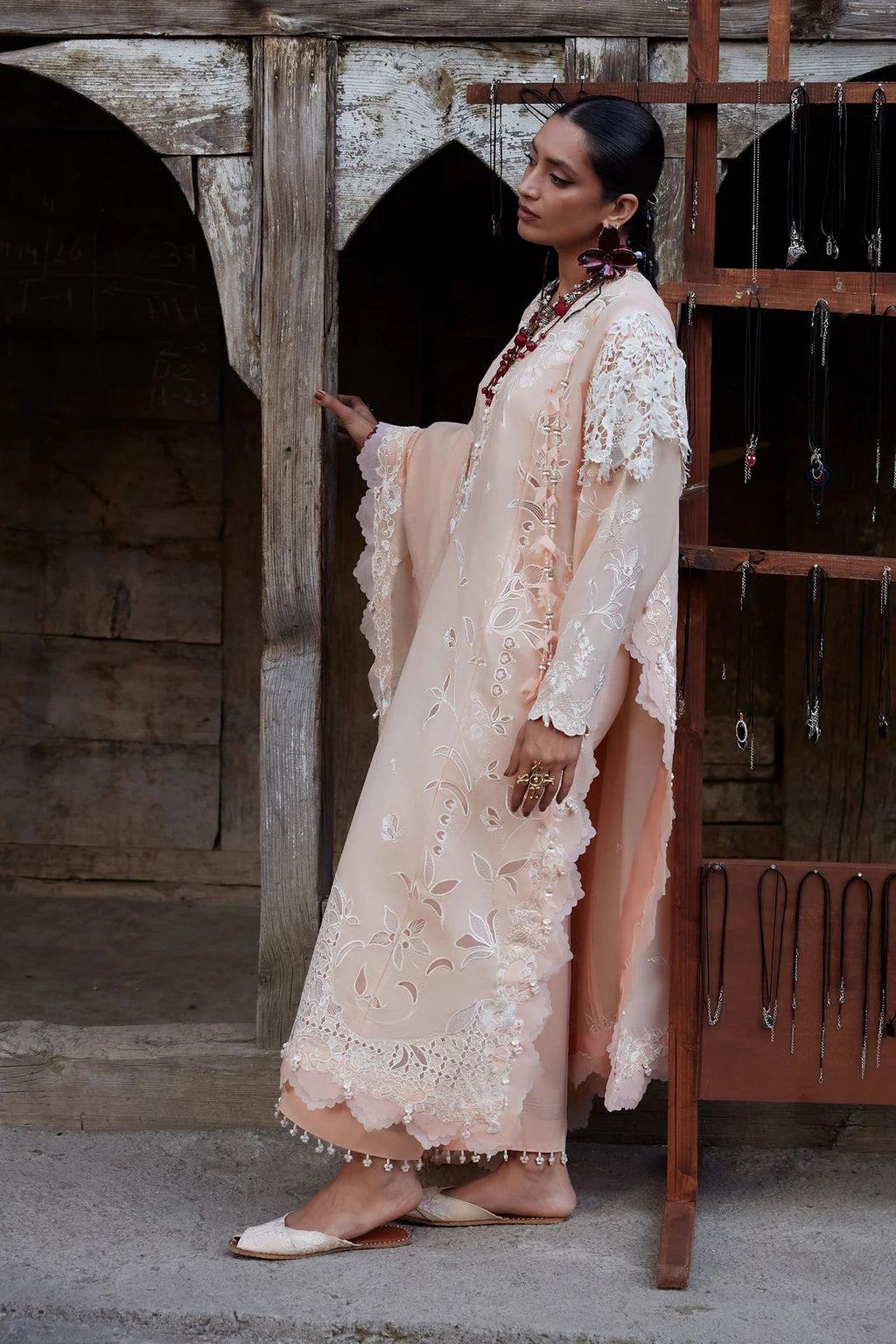 Woman in a beige lace dress standing in front of a rustic wooden door.