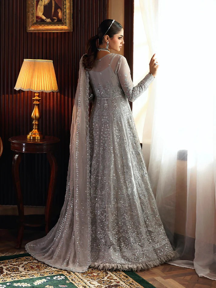 Woman in a silver embroidered gown standing in a room with a lamp and window.