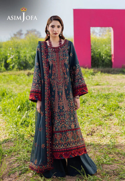 Woman wearing a patterned dress in a grassy field with a pink structure in the background, branded as Asim Jofa.