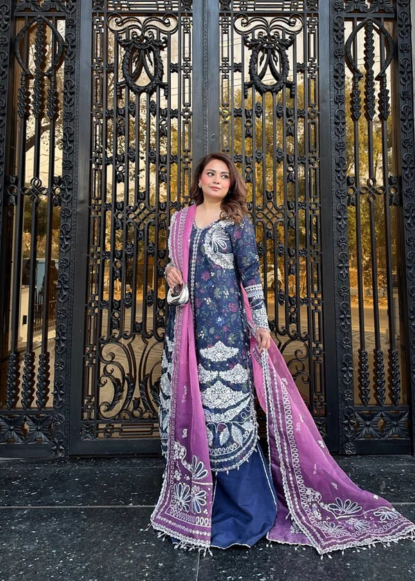 Woman in traditional outfit with purple dupatta standing in front of an ornate gate.