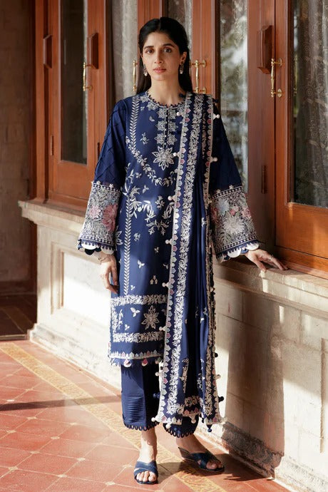 Woman in a blue traditional outfit with white patterns standing in front of a wooden door.