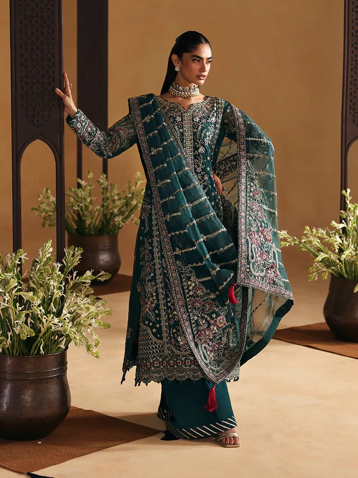 Woman in traditional embroidered outfit standing in a decorated room with plants.
