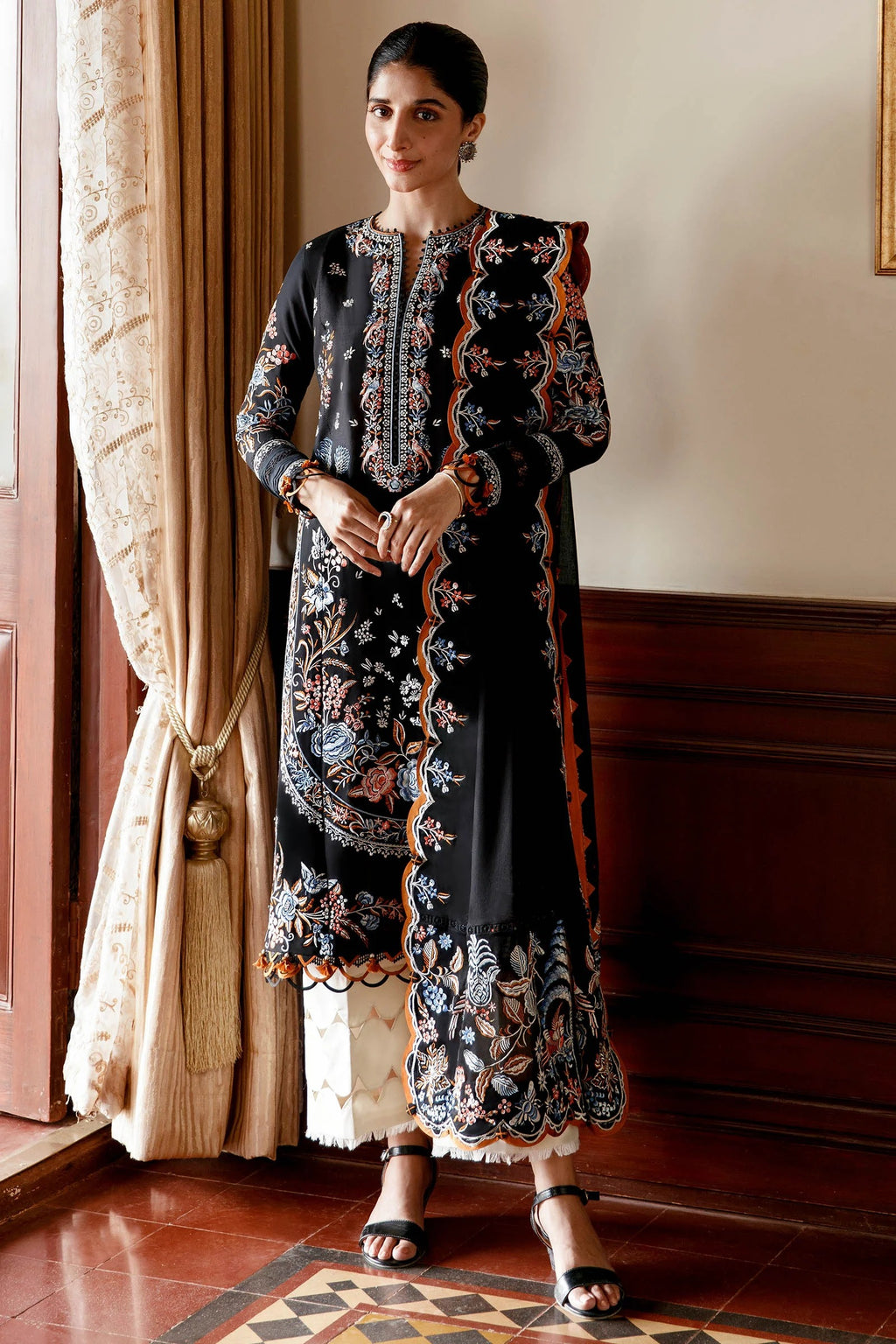Woman wearing a black embroidered traditional outfit in an elegant room.