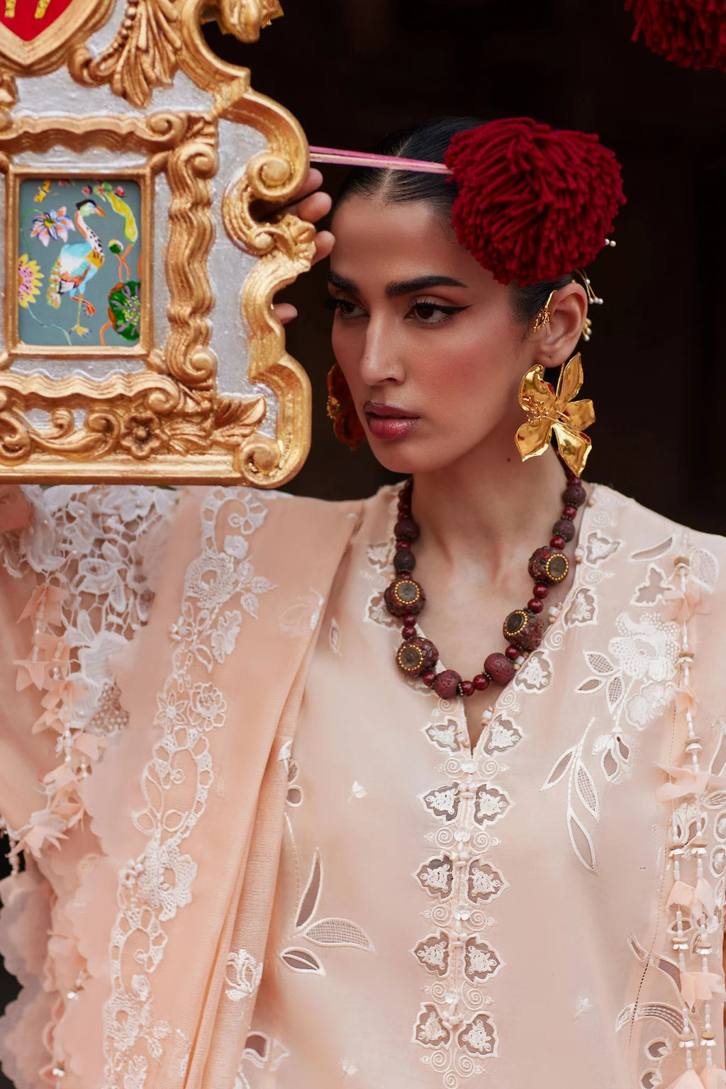 Woman in traditional attire with jewelry and a decorative headpiece, holding a mirror.