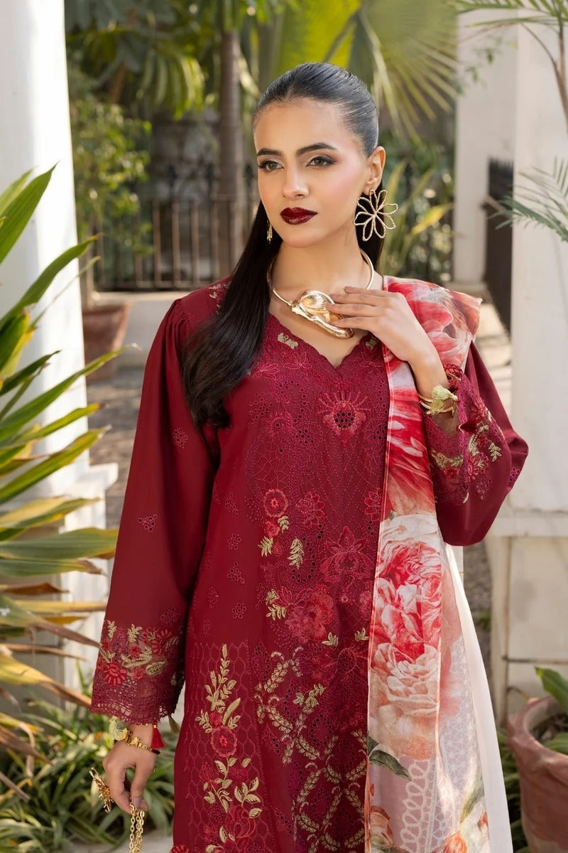 Woman wearing a red embroidered outfit with a floral scarf, standing outdoors with plants in the background.