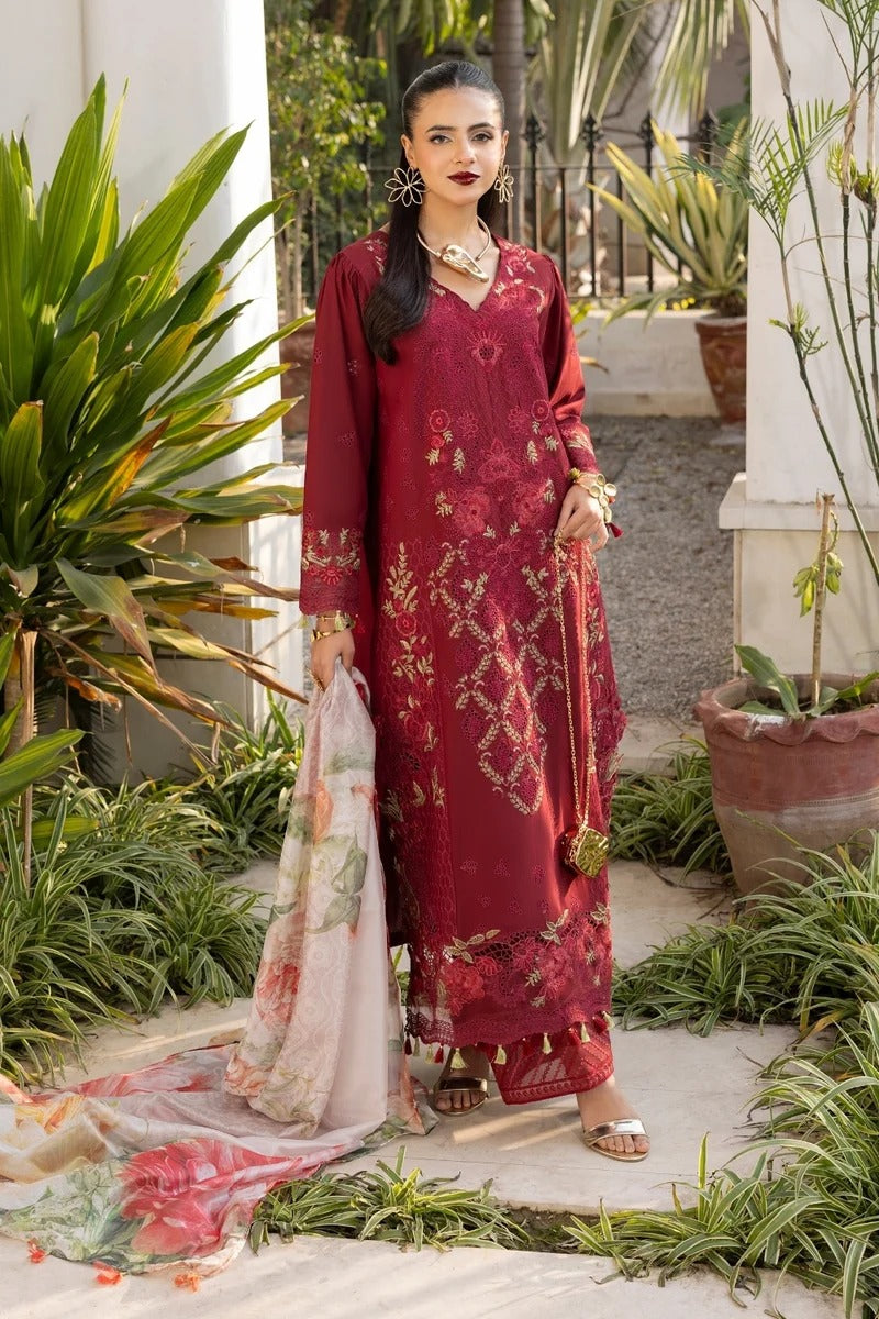 Woman in a red embroidered traditional outfit standing outdoors with plants around.