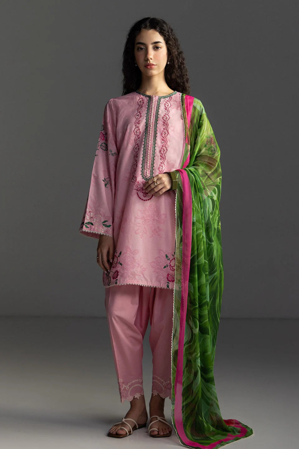 Woman wearing a pink embroidered outfit with a green dupatta against a gray background