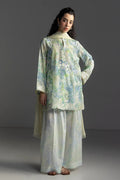 Woman wearing a floral blouse and light-colored pants against a gray background