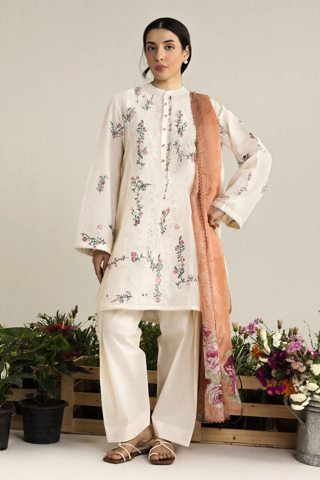 Woman wearing a floral embroidered outfit with a pink dupatta in a minimalistic setting.