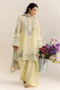 Woman in a light yellow embroidered outfit holding a bucket of flowers against a plain background