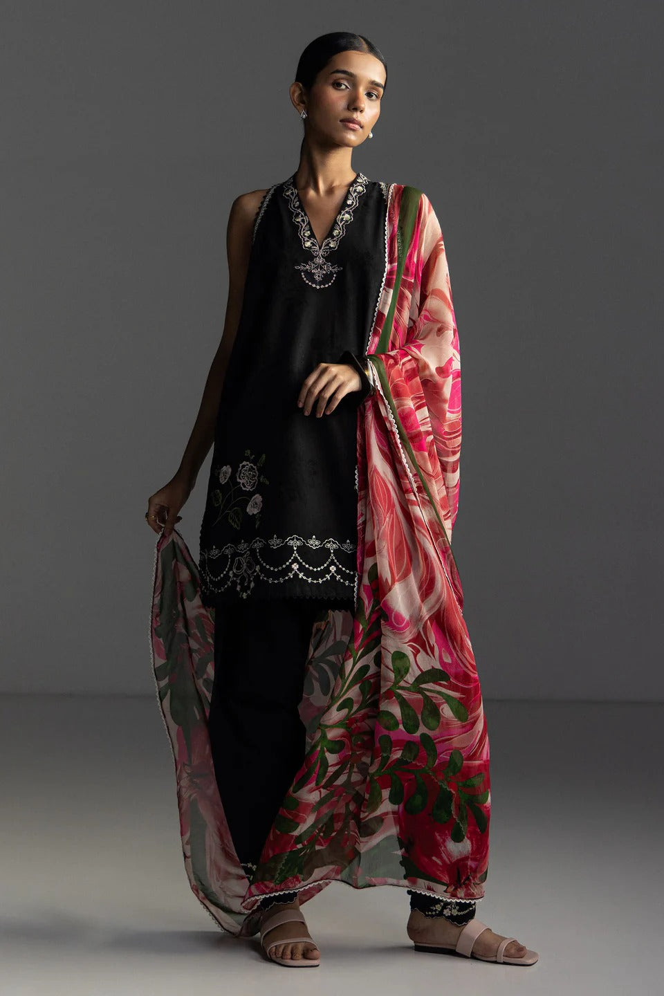 Woman wearing a black outfit with a pink floral dupatta against a gray background