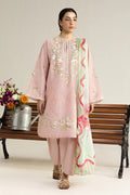 Woman in a pink embroidered outfit with a floral pattern, standing next to a wooden bench with flowers.