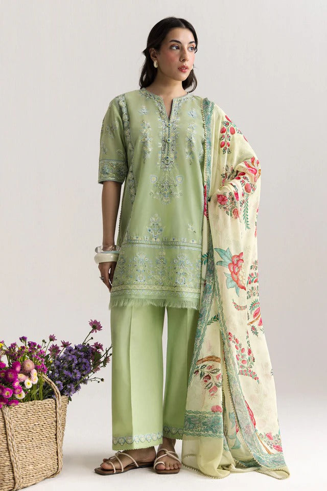 Woman wearing a light green traditional outfit with a floral dupatta, standing against a plain background.
