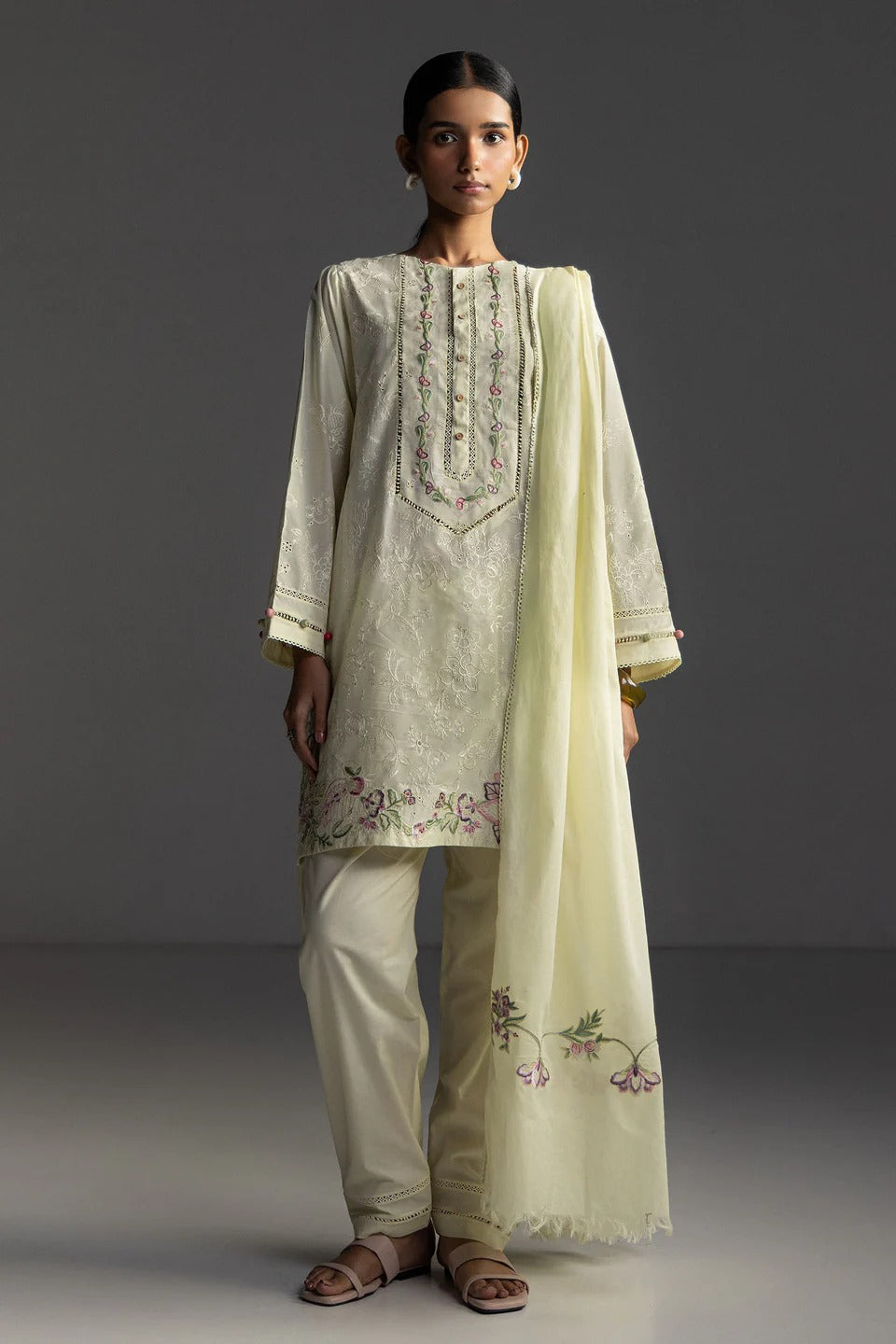 Woman wearing a traditional outfit with embroidered top and pants, holding a matching dupatta.