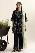 Woman wearing a black floral outfit with a green scarf, standing next to a wheelbarrow with plants.