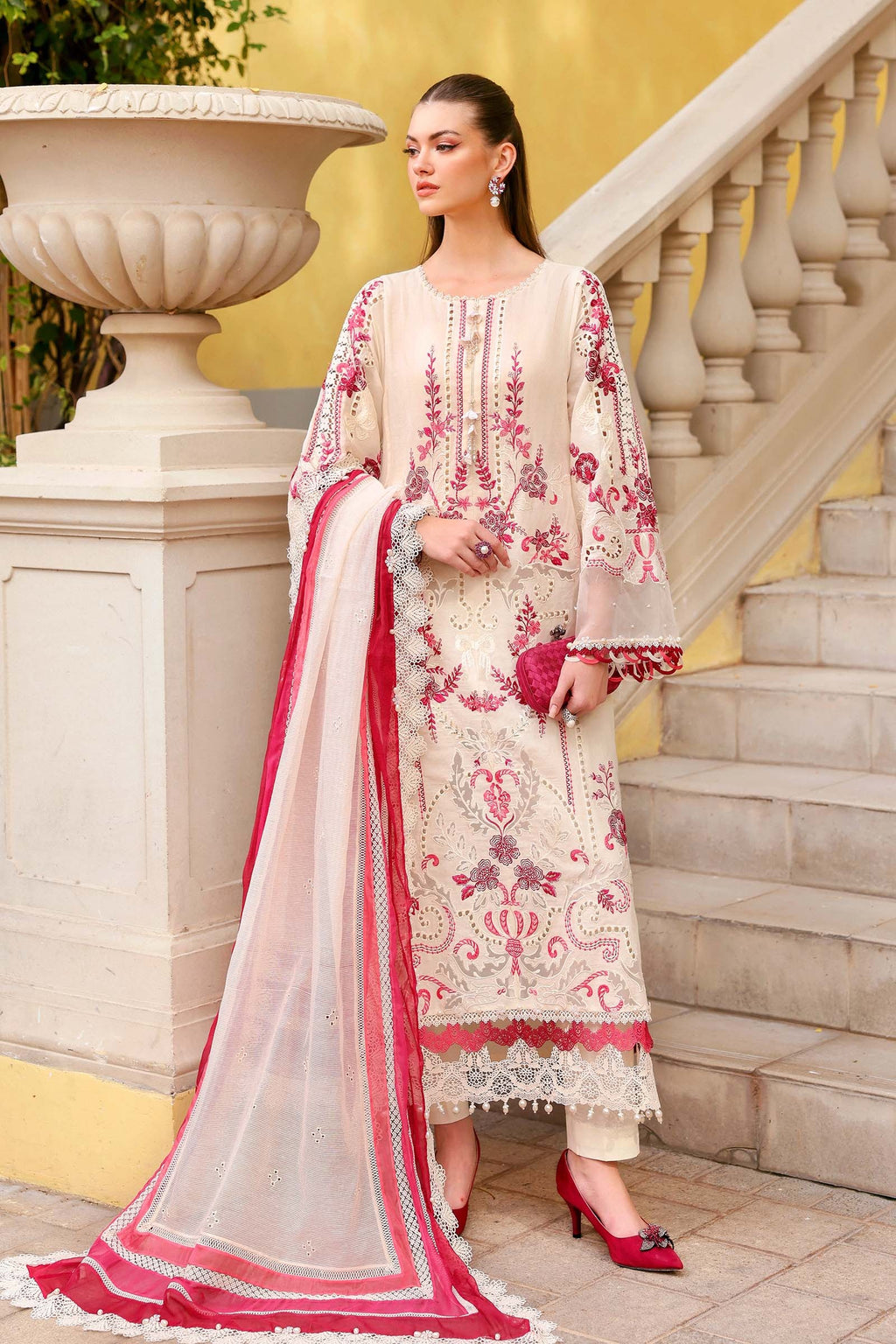 Woman in a traditional embroidered outfit standing on steps with a yellow wall in the background