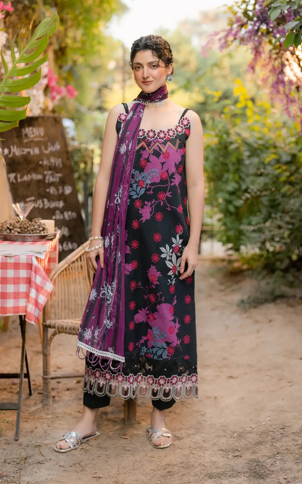 Woman in a floral dress standing outdoors with plants and a table in the background