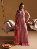 Woman in a pink embroidered traditional outfit standing in a decorated room with a swing and pillows.