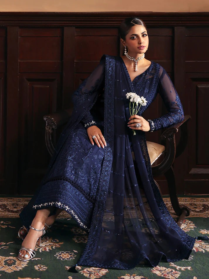 Woman in a dark blue saree holding flowers in a room with wooden paneling.
