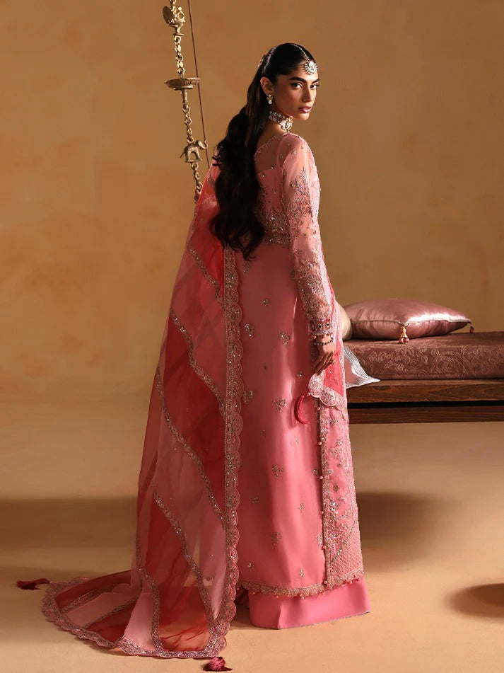 Woman in a pink traditional outfit with intricate designs, standing against a beige background.