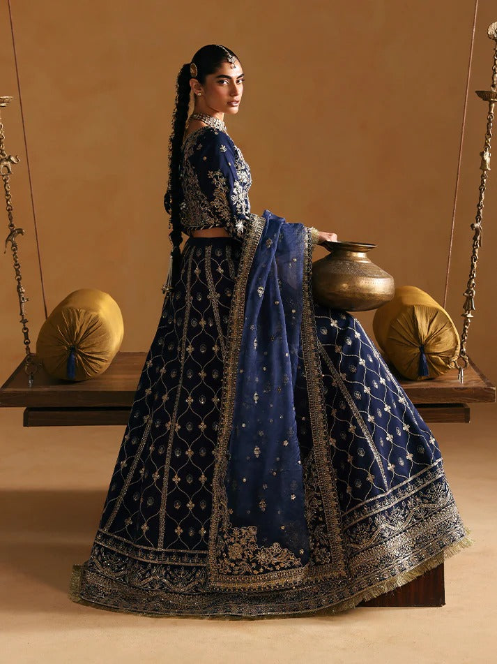 Woman in a traditional blue and black embroidered outfit holding a pot, standing on a swing.