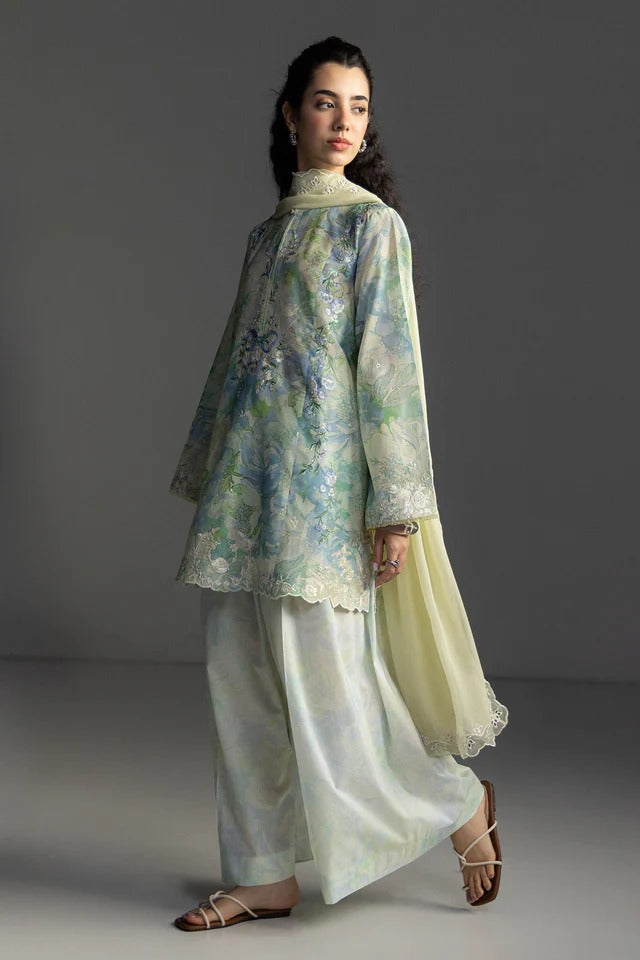 Woman wearing a floral blouse and light pants against a gray background