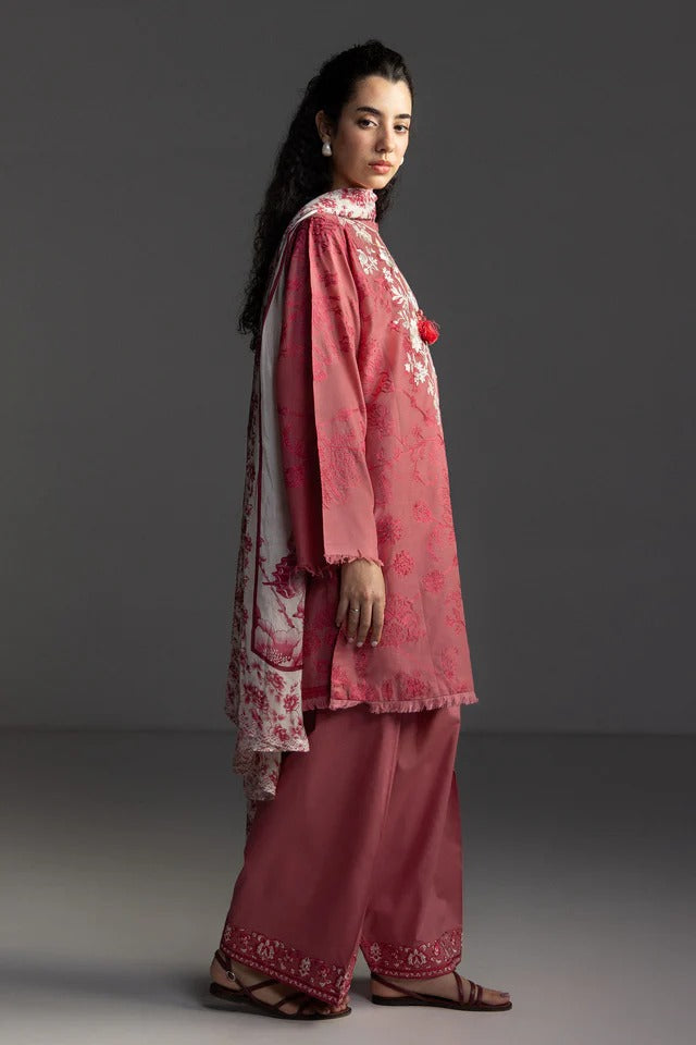 Woman wearing a traditional pink embroidered outfit on a gray background