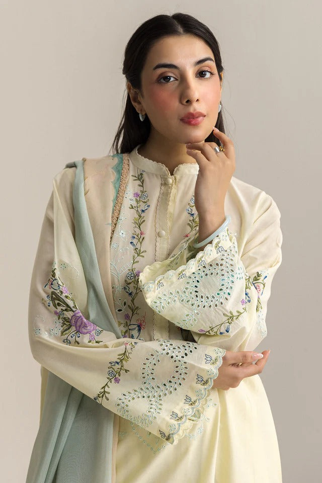 Woman wearing a cream-colored embroidered outfit with a matching shawl against a plain background