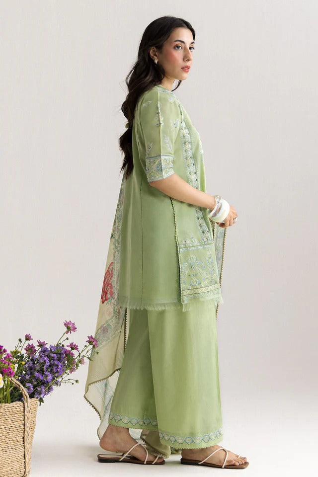 Woman wearing a light green traditional outfit with a floral dupatta, standing against a plain background.