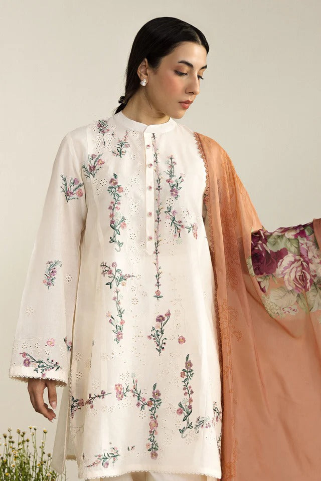 Woman wearing a white embroidered outfit with a peach dupatta against a neutral background