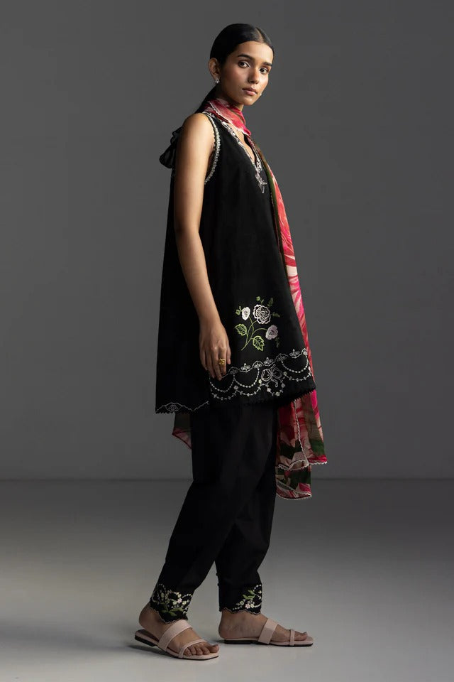 Woman wearing a black embroidered outfit with a pink dupatta on a gray background