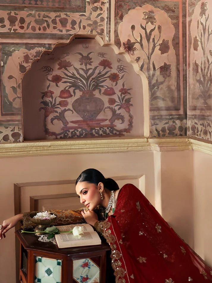 Woman in a red traditional outfit sitting in a decorated room with intricate wall art.
