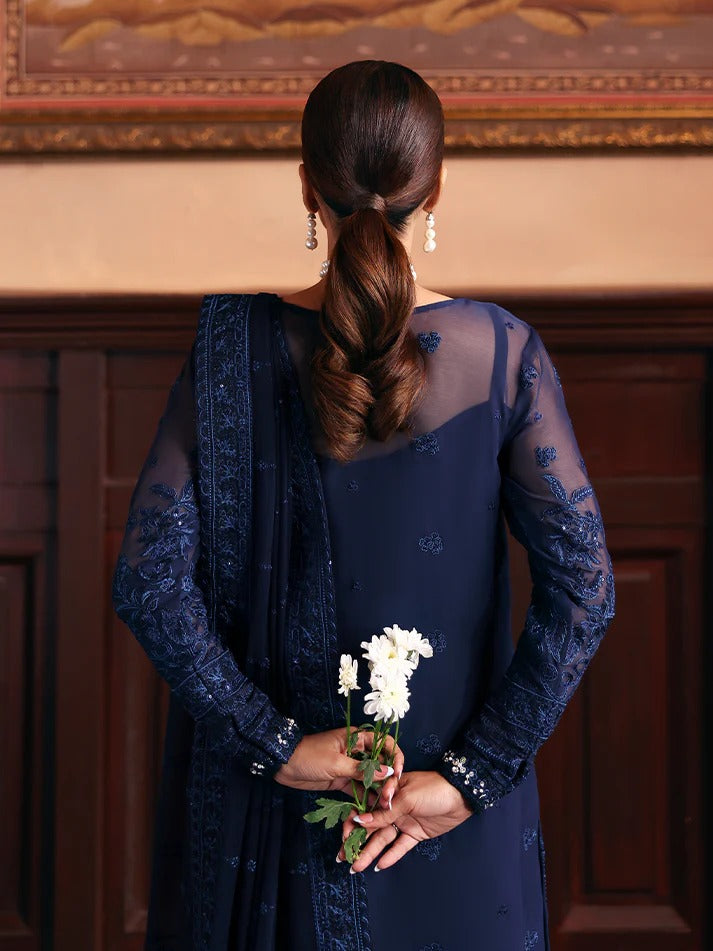 Woman in a navy blue dress holding flowers with a decorative wall in the background