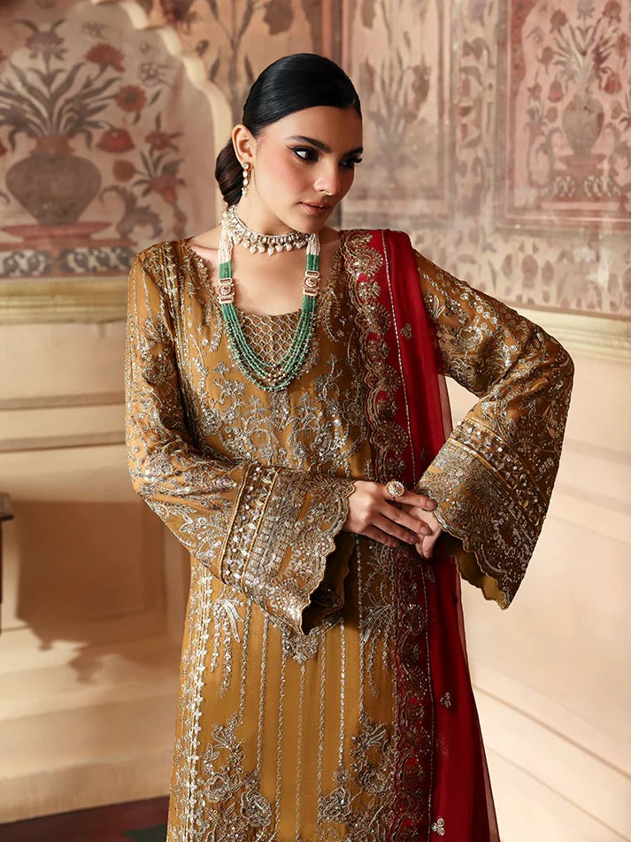 Woman in traditional embroidered outfit with red dupatta against a decorative wall.