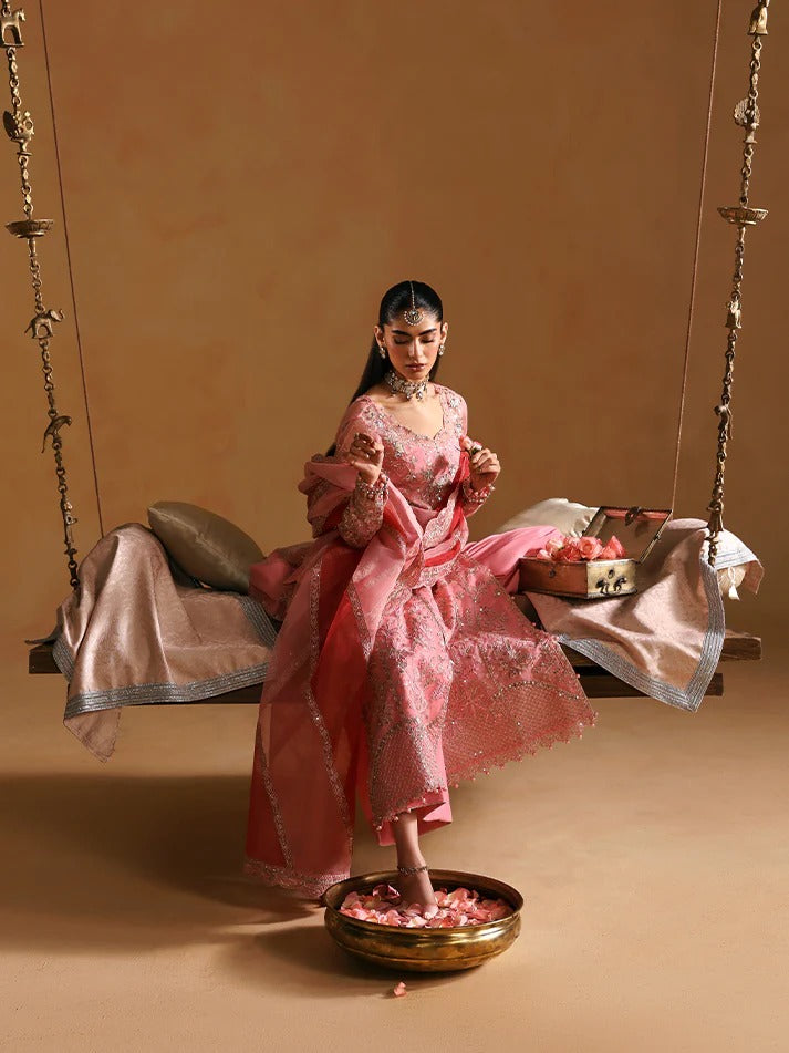 Woman in a pink traditional outfit standing next to a swing with a basket of flowers on a beige background