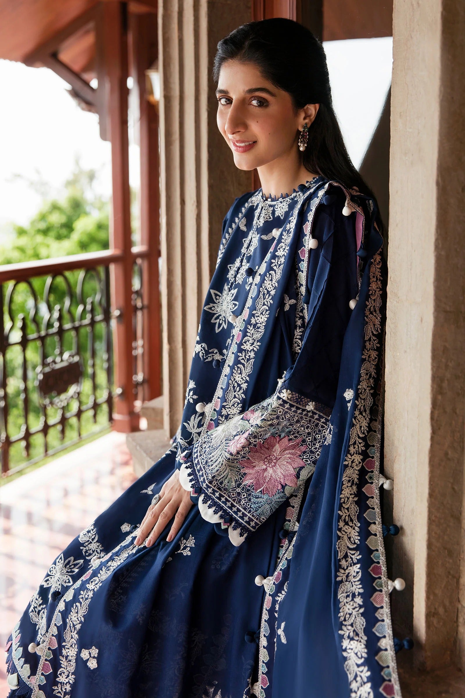 Woman in a blue embroidered traditional outfit standing on a balcony.